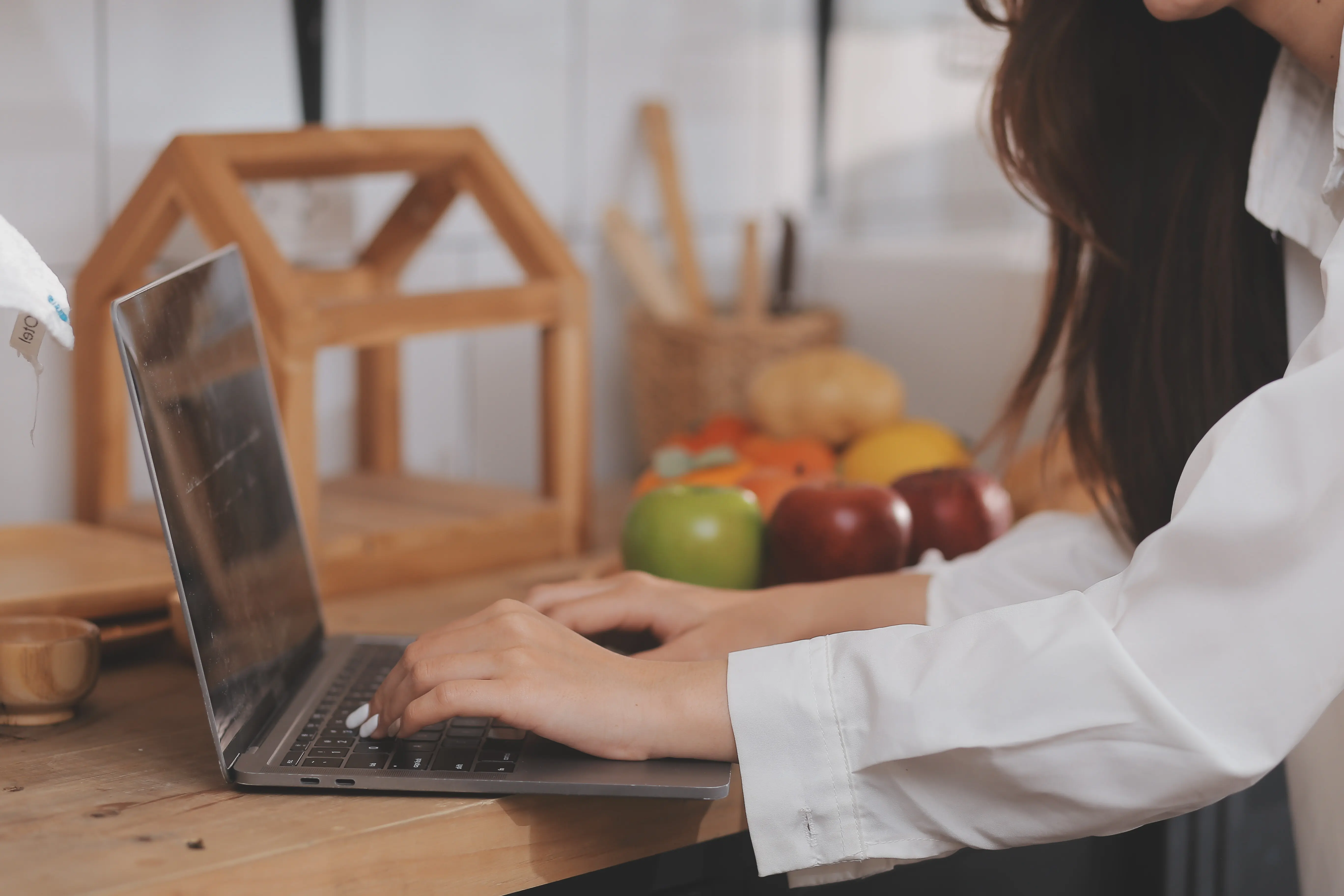Porträt einer hübschen, attraktiven, rothaarigen jungen Freelancerin, die im Homeoffice in der Küche am Tisch sitzt, arbeitet, auf einem Laptop tippt, lächelt und auf den Bildschirm schaut.